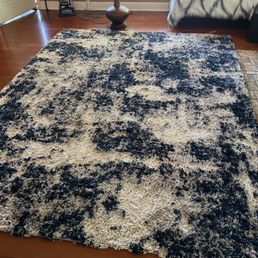 This is after and it looks like I just bought it. It's a two year old area rug. - A large, textured area rug with a black and white abstract pattern is placed on a wooden floor in a living room setting.