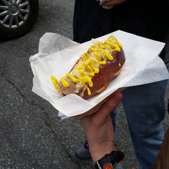 Federal City Brothers - a person holding a hot dog with mustard on it - Food Trucks Near Me Federal City Brothers - a person holding a hot dog with mustard on it - Food Trucks Near Me
