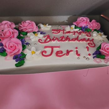 Bamboo Bakery - My cake from Bamboo Bakery. The photo doesn't do it justice. - A birthday cake with white icing decorated with pink roses, purple flowers, green leaves, and silver beads. The cake has a message written in pink icing that says 'Happy Birthday Teri!'. It is placed inside a pink box, with part of a metal shelf and a stainless steel container visible in the background. - Custom Cakes Near Me - Phoenix, Arizona