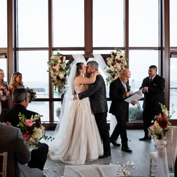 The NYC Wedding Photographer - The joyful first kiss as newlyweds at the altar, with guests applauding in an elegant waterfront ceremony venue. - Videographers Near Me - West Hempstead, New York The NYC Wedding Photographer - The joyful first kiss as newlyweds at the altar, with guests applauding in an elegant waterfront ceremony venue. - Videographers Near Me - West Hempstead, New York