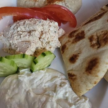 9 Muses - Three spreads - A plate featuring pita bread, sliced tomatoes, cucumber, chicken salad, and a creamy dip, with a bread roll in the background. - Greek Near Me - Chicago, Illinois