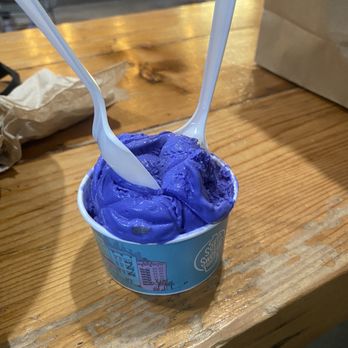 Soft Swerve - UBE butter cake - A small cup of purple Ube ice cream with two white plastic spoons, placed on a wooden table in an indoor setting. - Ice Cream & Frozen Yogurt Near Me - Brooklyn, New York