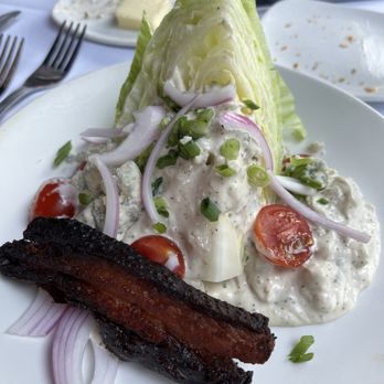 The Precinct - A salad featuring iceberg lettuce, cherry tomatoes, sliced onions, and a creamy dressing, with a piece of fried bacon on the side. - Steakhouses Near Me - Cincinnati, Ohio
