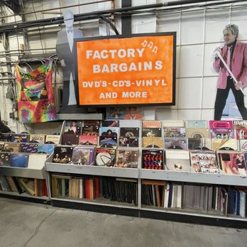 Factory Records - Vinyl records are displayed on a shelf at Factory Records, with a sign advertising bargains on DVDs, CDs, and vinyl. A cardboard cutout of a singer is positioned nearby. - Vinyl Records Near Me - Dover, New Jersey