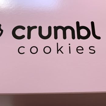 Crumbl - Naperville - The image features the Crumbl Cookies logo on a pink background. The logo includes a stylized cartoon chef's face with a chef's hat, positioned to the left of the text. The text 'crumbl' is written in bold, lowercase letters, with 'cookies' underneath in smaller, spaced-out lowercase letters. The surface appears to be a part of packaging or signage for the bakery. - Bakeries Near Me - Naperville, Illinois
