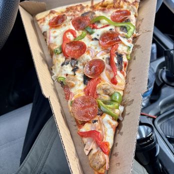 Slice Factory - Looks great! - A triangular slice of pizza with a thin crust, topped with pepperoni, sausage, red and green bell peppers, onions, and melted cheese, served in a cardboard pizza box. The pizza appears freshly baked with colorful toppings and is placed on a person's lap inside a vehicle. - Salad Near Me - River Grove, Illinois