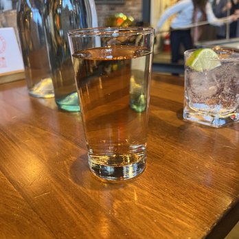 Fulton Hall - A tall glass of water with a lime wedge on the rim is placed on a wooden bar table, with water bottles and a glass of soda nearby. - Pubs Near Me - Brooklyn, New York
