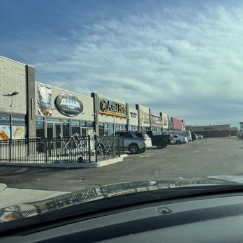 Asal Bee Cafe - A parking lot in front of a shopping plaza features multiple storefronts, including Asal Bee Cafe, with cars parked along the front. The sky is partly cloudy. - Coffee & Tea Near Me - Bridgeview, Illinois