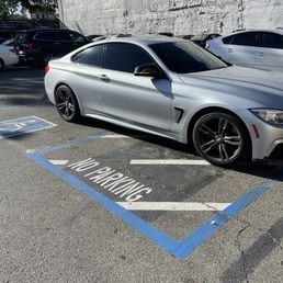 A silver car is parked horizontally across a handicapped parking spot A silver car is parked horizontally across a handicapped parking spot