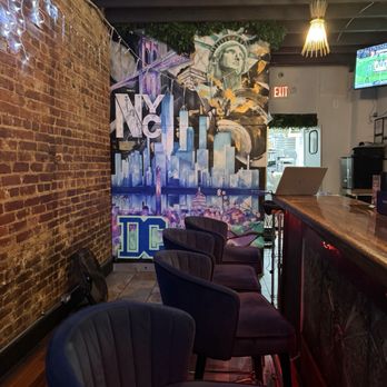 Mixxed DC - Bar interior featuring a NYC-themed mural, exposed brick wall, bar seating with velvet chairs, and decorative lighting. - Burgers Near Me - Washington, DC, District of Columbia