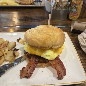 First Watch - A breakfast sandwich featuring bacon, scrambled eggs, and a biscuit is served on a white plate at a restaurant. - Breakfast & Brunch Near Me - Gilbert, Arizona