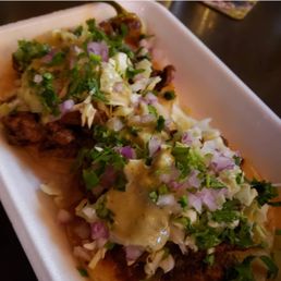 Birria tacos - A foam tray holds birria tacos garnished with chopped onions, cilantro, and sauce, served in a restaurant setting.