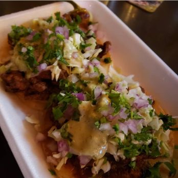 Bibi’s Latin Kitchen - Birria tacos - A foam tray holds birria tacos garnished with chopped onions, cilantro, and sauce, served in a restaurant setting. - Personal Chefs Near Me - Tempe, Arizona