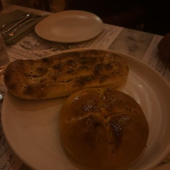 Eyval - Komaj + Babari breads - A white plate holds two Persian breads, one elongated and grilled, the other round and baked, on a restaurant table. - Persian/Iranian Near Me - Brooklyn, New York