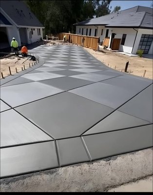 Modern Geometric Pattern Concrete Flatwork - Installation of a decorative concrete driveway and/or walkway featuring a modern, geometric design. The concrete surface is finished smooth, with precisely placed sawcut or tooled control joints forming large rectangular and angular patterns. This approach not only increases the aesthetic appeal with a contemporary, custom look, but also enhances the durability and performance of the slab by controlling cracking. The final product provides a clean, high-end appearance that complements modern residential and commercial properties.