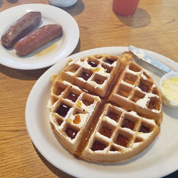 Francoeur's Cafe - Belgian waffle w/ real syrup & hot sausage. - Belgian waffle with syrup served on a white plate, accompanied by a small cup of butter and a side of sausage links on a separate plate. - Breakfast & Brunch Near Me - Manchester, New Hampshire