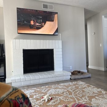 24K CCTV - The image shows a living room with a mounted TV above a white brick fireplace, a dog lying on a bed to the right, and a patterned rug on the floor. - Security Systems Near Me