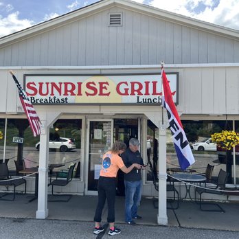 Sunrise Grill - two people standing in front of a restaurant - Sunrise Grill's exterior features a sign, American flags, and hanging flower baskets, with two people standing outside near the entrance. - American Near Me - Kittery, Maine