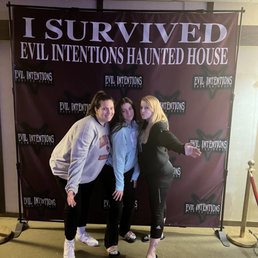 Another photo area - Three women stand in front of a dark backdrop with the text "I Survived Evil Intentions Haunted House," at a haunted attraction event.