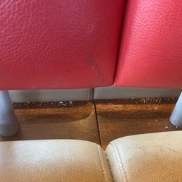 a close up of a red leather chair - The image shows the lower parts of red and beige chairs with metal legs on a wooden floor, with some debris and scuff marks.