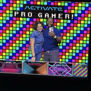 Activate Games - Photo Booth - A man and woman pose for a selfie in front of a vibrant, pixel art-style background at Activate Games, a gaming venue. - Arcades Near Me - Cincinnati, Ohio