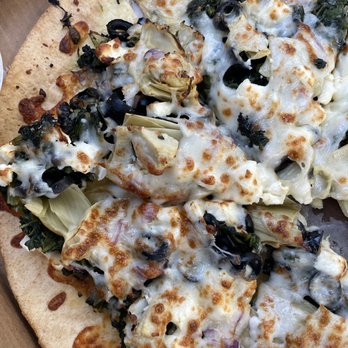 Davidos - a pizza in a pizza box - A close-up image of a pizza with a golden-brown crust, topped with melted cheese, black olives, artichoke hearts, and leafy greens. The pizza is placed inside a cardboard box, indicating it is for takeout or delivery. The toppings are spread evenly across the surface, with some areas showing slightly browned cheese. - Pizza Near Me - Rio Rancho, New Mexico