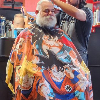 Campus Barber - Zack is one of the best barbers in the shop - A barber is cutting a customer's hair in a barbershop, with the customer wearing a cape featuring Dragon Ball characters. - Barbers Near Me - Albuquerque, New Mexico