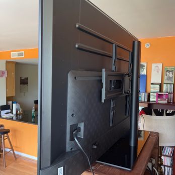 Transcend Home Theater - A flat-screen TV is mounted on a wooden table, showing its rear side with mounting brackets and a power cord. - Home Theatre Installation Near Me - Potomac, Maryland