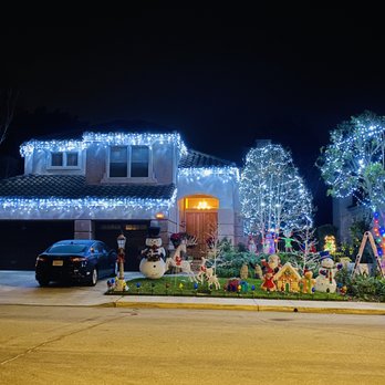 Illuminating Team - A residential house is illuminated with white Christmas lights on the roof, trees, and around the entrance, with holiday yard decorations including snowmen, reindeer, and a gingerbread house. - Lighting Fixtures & Equipment Near Me