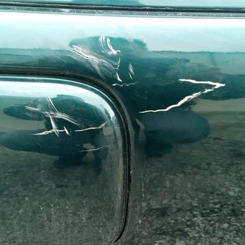 Integrity Automotive - This happened after the initial first six days, but before it was finished. - A green vehicle's rear bumper displays multiple scratches and dents, indicating minor damage. The license plate is partially visible, showing the number 43 and an Illinois registration sticker. The bumper's surface reflects the surroundings, including the person taking the photo and the ground beneath the vehicle. - Auto Repair Near Me - Minooka, Illinois