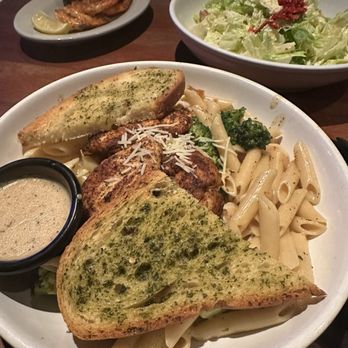 Jasper's - Spicy Shrimp & Chicken Pasta - A pasta dish with garlic bread, grilled chicken, and vegetables is served on a white plate, accompanied by a side salad and chicken wings in the background. - American Near Me - Upper Marlboro, Maryland