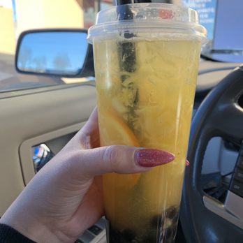 Hi Boba - Hawaiian Fruit Tea with boba - A person holds a large plastic cup of yellow fruit tea with boba, inside a vehicle with a beige interior and side mirror visible. - Coffee & Tea Near Me - Rio Rancho, New Mexico