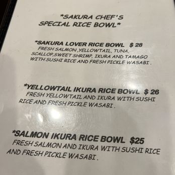 Sakura Grill - A menu from Sakura Grill in Burke, VA, displays three rice bowl options: Sakura Lover Rice Bowl for $28, Yellowtail Ikura Rice Bowl for $26, and Salmon Ikura Rice Bowl for $25. Each item includes ingredients like fresh salmon, yellowtail, tuna, ikura, sushi rice, and pickles, with descriptions emphasizing the freshness and ingredients used. The menu is printed on white paper with bold, black text, and is part of a restaurant setting. - Sushi Bars Near Me - Burke, Virginia