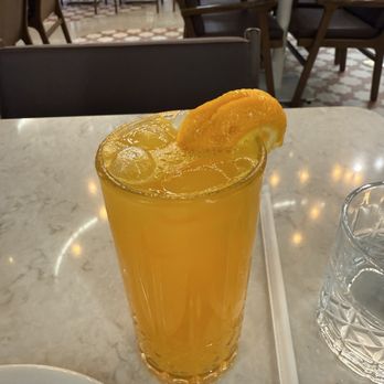 Moda Cafe and Restaurant - Fresh Orange Juice - A glass of orange juice with ice and a lemon wedge on top is placed on a marble table in a restaurant setting. - Turkish Near Me - Chantilly, Virginia