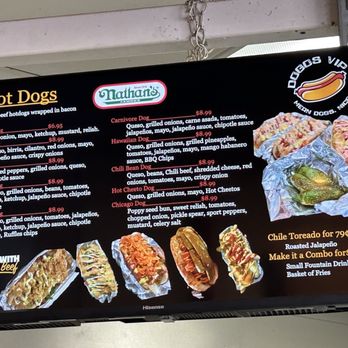 Dogos VIP - Menu board - Digital menu board at Dogos VIP in Albuquerque, NM, featuring a list of hot dogs such as Classic, Birria, Philly, Sonora, Crunch, Carnivore, Hawaiian, Chili Bean, Hot Cheeto, and Chicago, each with detailed ingredients and prices. The board also promotes Chile Toreado for 79 cents, combo deals, and beverages like fountain drinks and basket of fries. The menu emphasizes the use of 100% beef and includes images of hot dogs with toppings. - Hot Dogs Near Me - Albuquerque, New Mexico