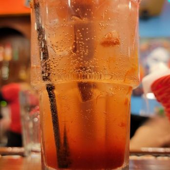 La Mision - A beverage in a tall glass with bubbles, a salted rim, and a yellow straw, set on a wooden table in a lively restaurant environment. - Mexican Near Me - Midland, Texas