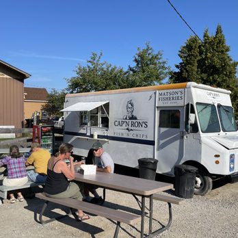 Cap’n Ron’s Fish and Chips - ows people sitting at a picnic table in front of a food truck - Fish & Chips Near Me - Munising, Michigan