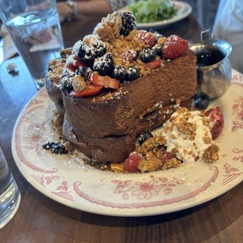 Eggstasy - French toast - A thick slice of French toast topped with mixed berries, powdered sugar, and granola, served with syrup and whipped cream on a floral-patterned plate. - Breakfast & Brunch Near Me - Mesa, Arizona