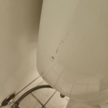 Kleen - Stain on the side of the toilet that remained but was easy to wipe off myself. - The image shows a close-up of a white toilet in a bathroom setting. The toilet has visible brown stains and dirt marks on its surface, particularly near the tank. The bathroom floor is tiled with square tiles, and plumbing pipes are visible at the base of the toilet, connecting it to the wall. The lighting appears to be artificial, casting a neutral tone over the scene. - Home Cleaning Near Me - Pasadena, California