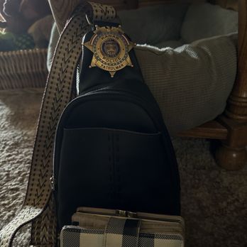 JCPenney - A police badge labeled 'Kanab Police Patrolman' is attached to a strap on a black backpack, placed on a wooden chair inside a room. - Department Stores Near Me - Flagstaff, Arizona