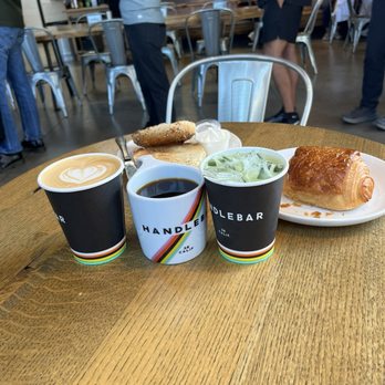 Handlebar Coffee Roasters - Medium roast coffee, Vanilla latte and iced matcha in to-go cups.Everything bagel and chocolate croissant in the background. - Coffee Roasteries Near Me - Santa Barbara, California