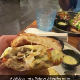 Torta de chilaquiles , cut In half. Some of the sauces can be seen on plate Torta de chilaquiles , cut In half. Some of the sauces can be seen on plate