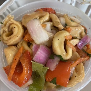 Gansett Wraps - Tortellini - The image shows a plastic container filled with tortellini pasta combined with chopped vegetables including red onions, carrots, and green peppers. The pasta appears coated in a light sauce or dressing, and the vegetables are cut into small pieces. The container is placed on a surface, possibly for takeout or delivery, with part of a white napkin visible in the background. - Mediterranean Near Me - Westerly, Rhode Island