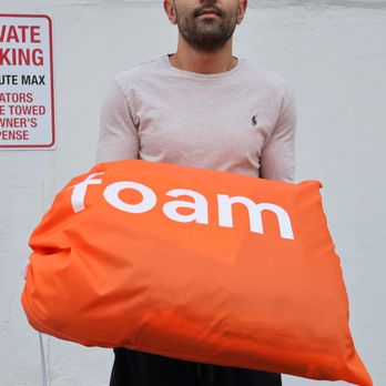 Foam Laundry - Happy customer holding a bright orange foam bag outside their apartment. - Laundromat Near Me Foam Laundry - Happy customer holding a bright orange foam bag outside their apartment. - Laundromat Near Me