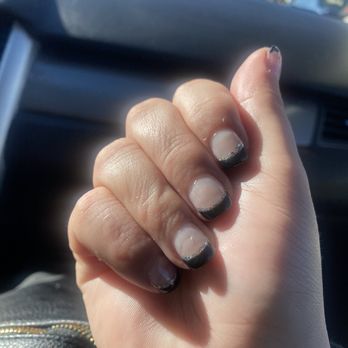 Luxury Nails and Spa - uneven i even have the red still on my nail from my last color they look horrible i have short nails so French tip should be thinner - Close-up of a person's hand with short nails, painted with black and silver French tips, inside a vehicle. The background shows a blurred view of traffic and vehicles through the windshield, indicating the photo was taken while in a car. The nails are neatly manicured, and the skin appears smooth. The image captures the hand prominently, with the car's interior visible around it. - Hair Removal Near Me - Albuquerque, New Mexico