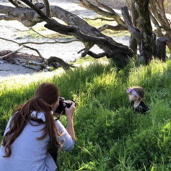 The Wild Bloom Studio - Meghan taking a photo of a little girl wearing a bow in a grassy clearing near a beach - Session Photography Near Me - Cupertino, California