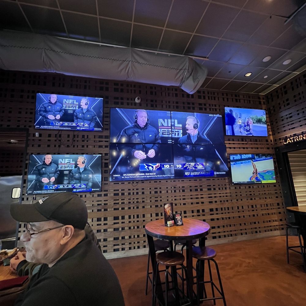 Bombshells Restaurant & Bar - a man sitting at a table and watching tvs - Sports Bars Near Me - Pearland, Texas
