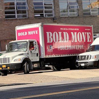Bold Move - One of the Bold Move moving trucks - A white moving truck with pink branding for Bold Move is parked on a city street, with a brick building and other vehicles nearby. - Movers Near Me - Portland, Oregon