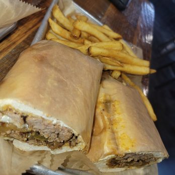 Bobby Mcgee’s - Philly cheesesteak and fries - A Philly cheesesteak sandwich with melted cheese and cooked meat, served with French fries on a metal tray at a restaurant. - Bars Near Me - Fort Wayne, Indiana