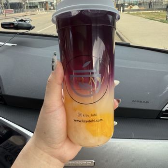 Krav Cafe - lychee butterfly - A person holds a large iced beverage with a gradient color from yellow to dark purple, inside a car. The drink features a logo and website for Krav LoHi. - Cafes Near Me - Denver, Colorado